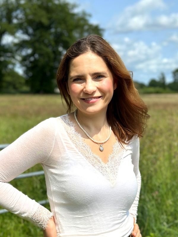 Irina Bork auf einer Wiese, die Hände in die Hüften gestützt, lachend